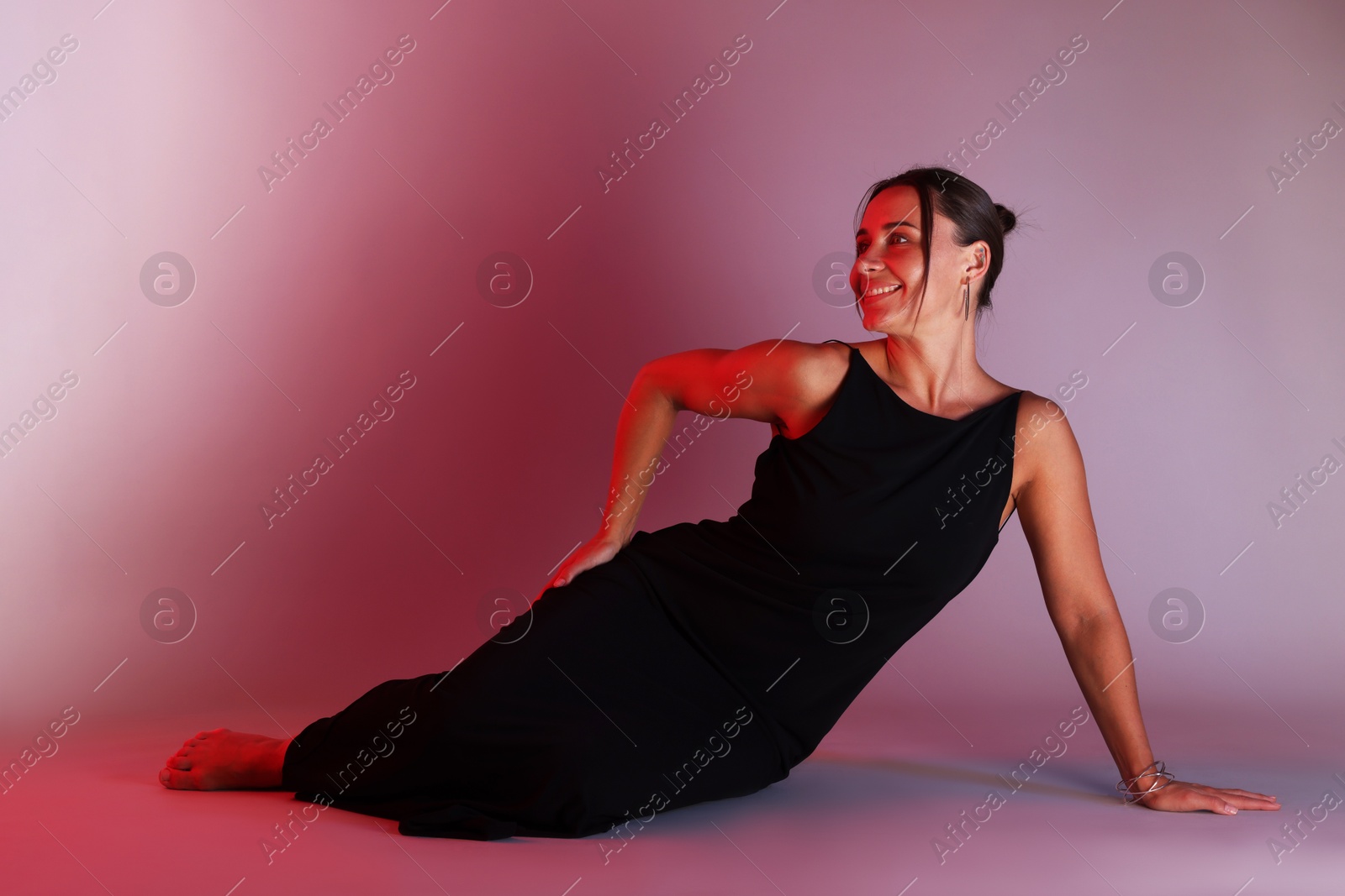 Smiling woman wearing dress posing in neon lights against color background Photo of Smiling woman wearing dress posing in neon lights against color background