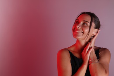 Photo of Smiling woman with bracelet in neon lights against color background. Space for text