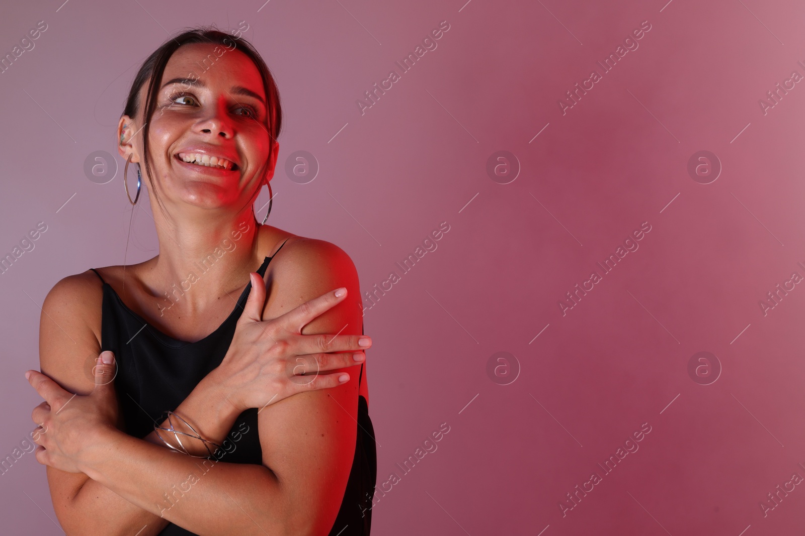 Smiling woman in neon lights against color background. Space for text Photo of Smiling woman in neon lights against color background. Space for text