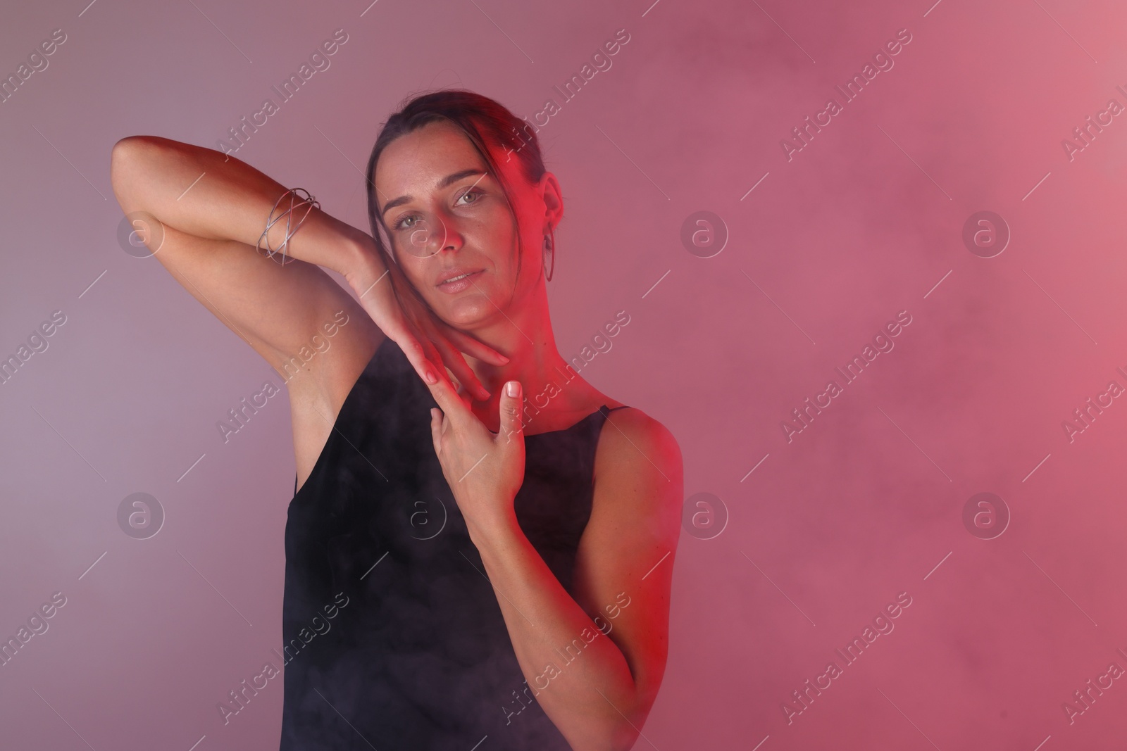 Portrait of beautiful woman with bracelet in neon lights and smoke against color background. Space for text Photo of Portrait of beautiful woman with bracelet in neon lights and smoke against color background. Space for text