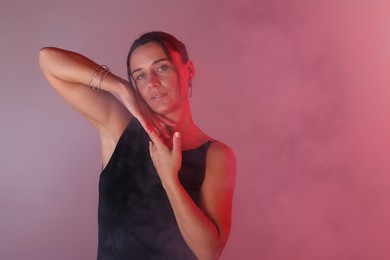 Photo of Portrait of beautiful woman with bracelet in neon lights and smoke against color background. Space for text