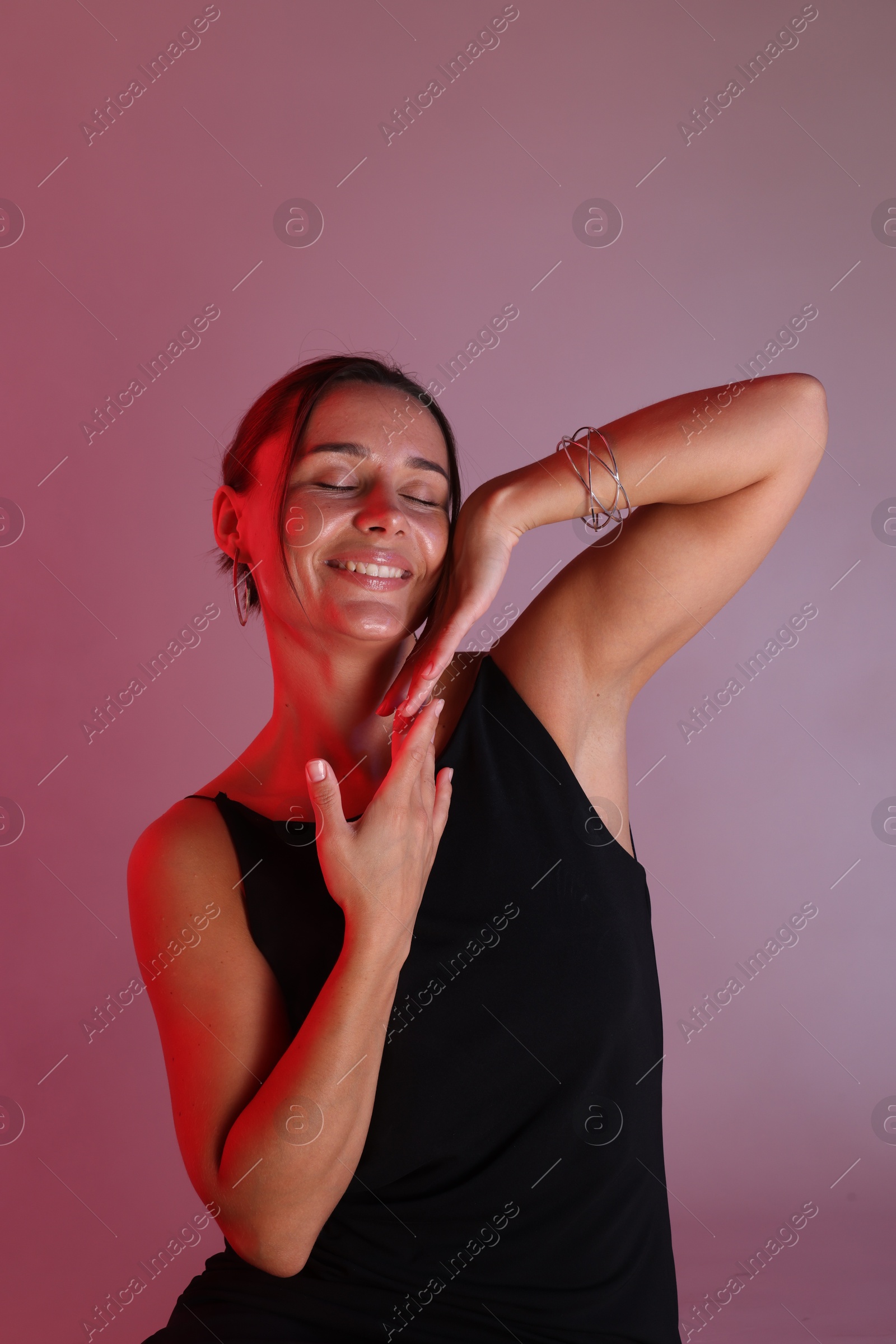 Smiling woman with bracelet in neon lights against color background Photo of Smiling woman with bracelet in neon lights against color background