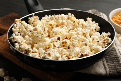 Photo of Tasty popcorn in frying pan on black table, closeup