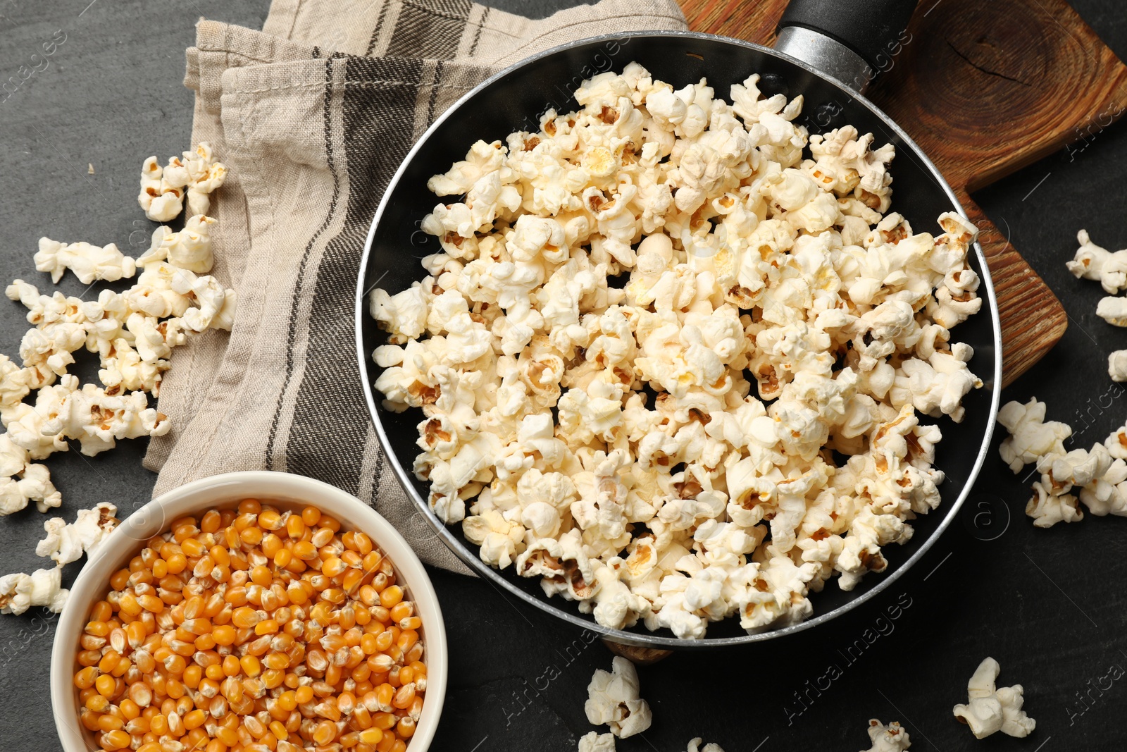 Tasty popcorn in frying pan and corn kernels on black table, flat lay Photo of Tasty popcorn in frying pan and corn kernels on black table, flat lay