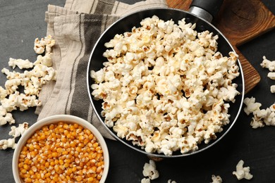 Photo of Tasty popcorn in frying pan and corn kernels on black table, flat lay