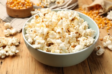 Photo of Tasty popcorn and corn kernels on wooden table, closeup