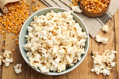 Photo of Tasty popcorn and corn kernels on wooden table, flat lay