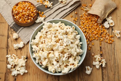 Photo of Tasty popcorn and corn kernels on wooden table, flat lay
