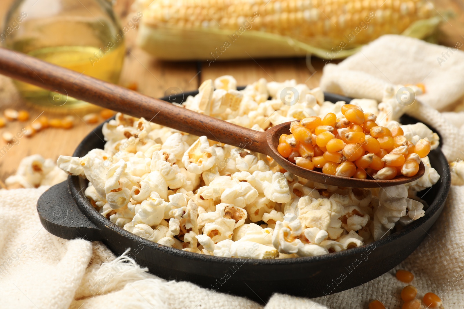 Photo of Tasty popcorn, corn kernels, oil and towel on wooden table, closeup