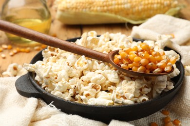 Photo of Tasty popcorn, corn kernels, oil and towel on wooden table, closeup
