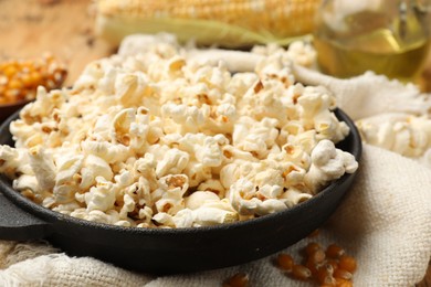 Photo of Tasty popcorn, corn kernels, oil and towel on wooden table, closeup