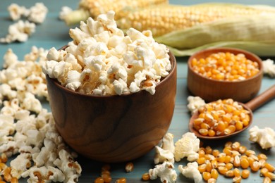 Photo of Tasty popcorn and corn kernels on blue wooden table, closeup