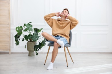 Photo of Happy man listening to music in headphones on chair at home