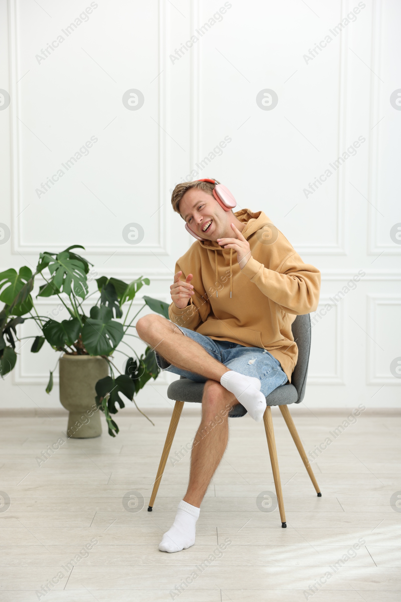 Happy man listening to music in headphones on chair at home Photo of Happy man listening to music in headphones on chair at home