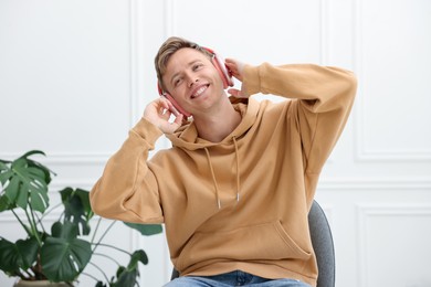 Photo of Happy man listening to music in headphones on chair at home