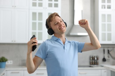 Photo of Happy man with smartphone listening to music in headphones and dancing at home