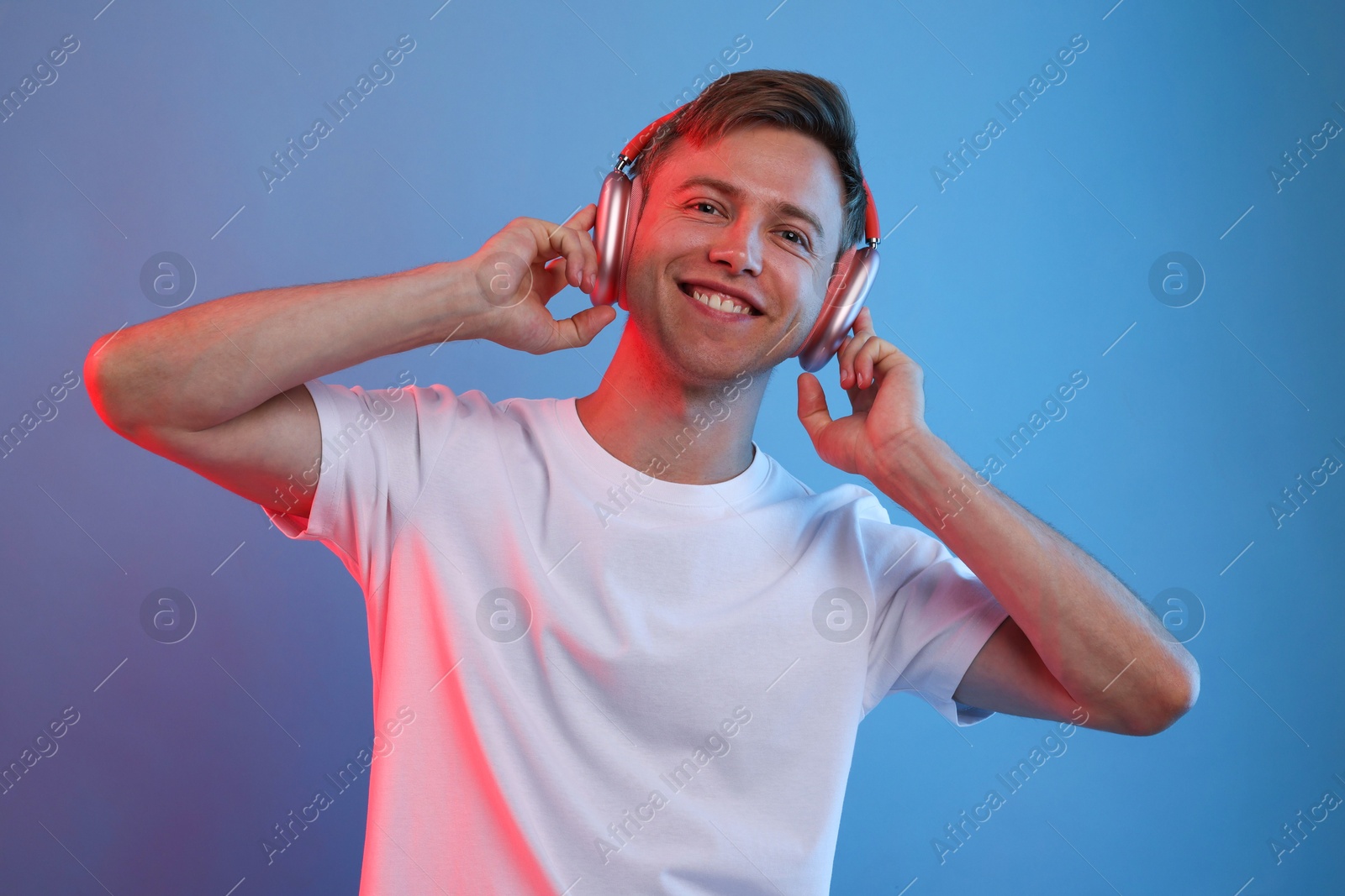 Happy man listening to music in headphones on blue background with neon light Photo of Happy man listening to music in headphones on blue background with neon light