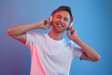 Photo of Happy man listening to music in headphones on blue background with neon light