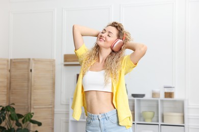 Photo of Happy woman in headphones listening to music and dancing at home