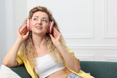Photo of Happy woman listening to music in headphones on sofa at home. Space for text