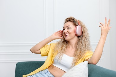Photo of Happy woman listening to music in headphones on sofa at home. Space for text