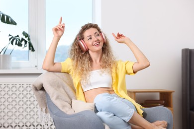 Photo of Happy woman with headphones listening to music in armchair at home