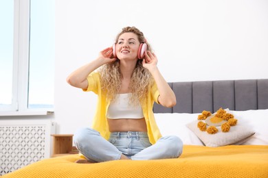 Photo of Happy woman listening to music in headphones on bed at home