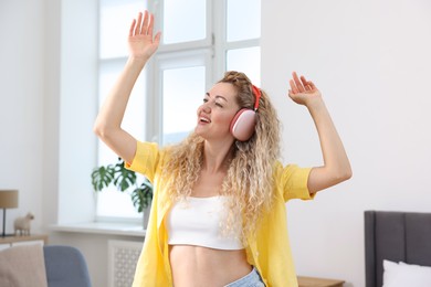 Photo of Happy woman in headphones listening to music and dancing at home