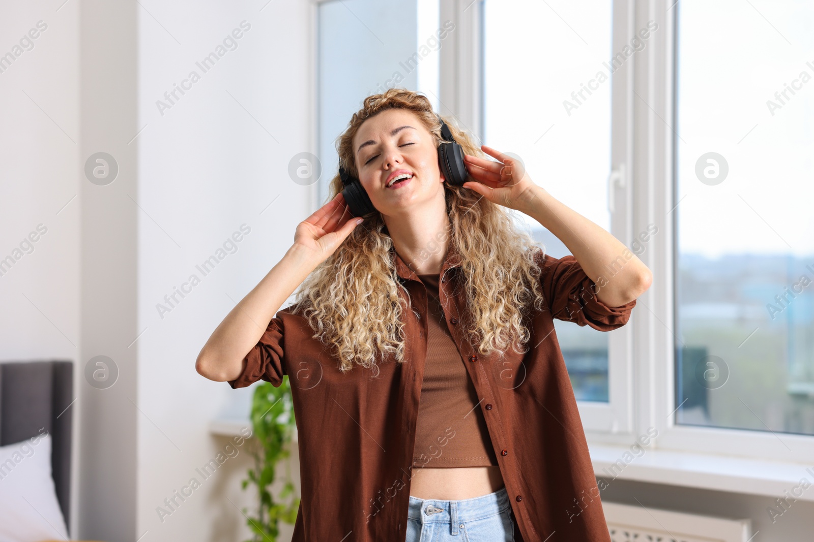 Photo of Happy woman in headphones listening to music and dancing at home