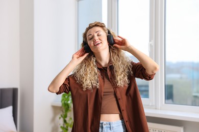 Photo of Happy woman in headphones listening to music and dancing at home