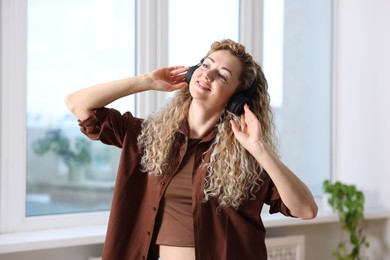 Photo of Happy woman in headphones listening to music and dancing at home