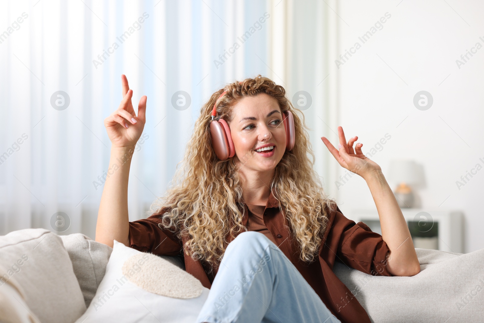 Photo of Happy woman listening to music in headphones on sofa at home