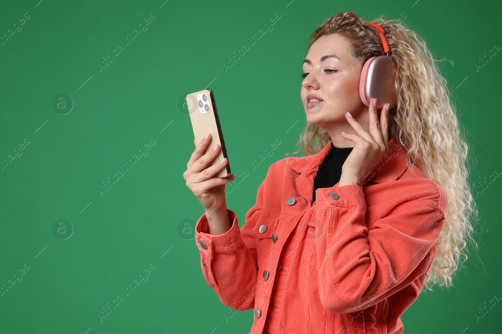 Happy woman with smartphone listening to music in headphones on green background. Space for text Photo of Happy woman with smartphone listening to music in headphones on green background. Space for text