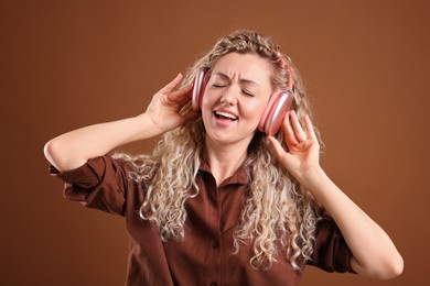 Photo of Happy woman listening to music in headphones and dancing on brown background