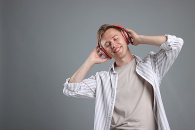Photo of Happy man listening to music in headphones and dancing on grey background. Space for text