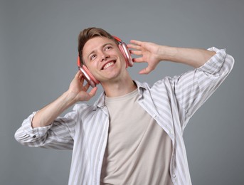 Photo of Happy man listening to music in headphones and dancing on grey background