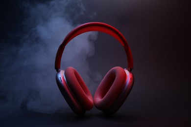 Photo of Pair of wireless headphones on dark background with color lights and smoke
