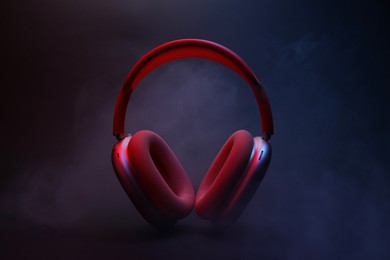 Photo of Pair of wireless headphones on dark background with color lights and smoke