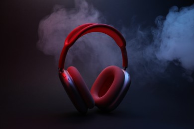 Photo of Pair of wireless headphones on dark background with color lights and smoke