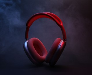 Photo of Pair of wireless headphones on dark background with color lights and smoke