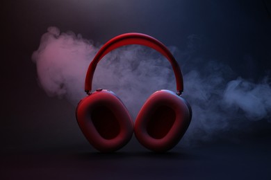 Photo of Pair of wireless headphones on dark background with color lights and smoke