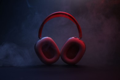 Photo of Pair of wireless headphones on dark background with color lights and smoke