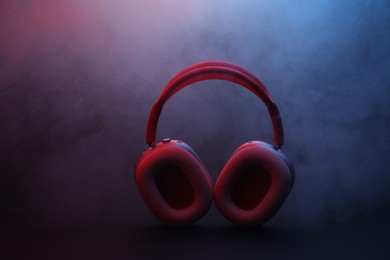 Photo of Pair of wireless headphones on dark background with color lights and smoke