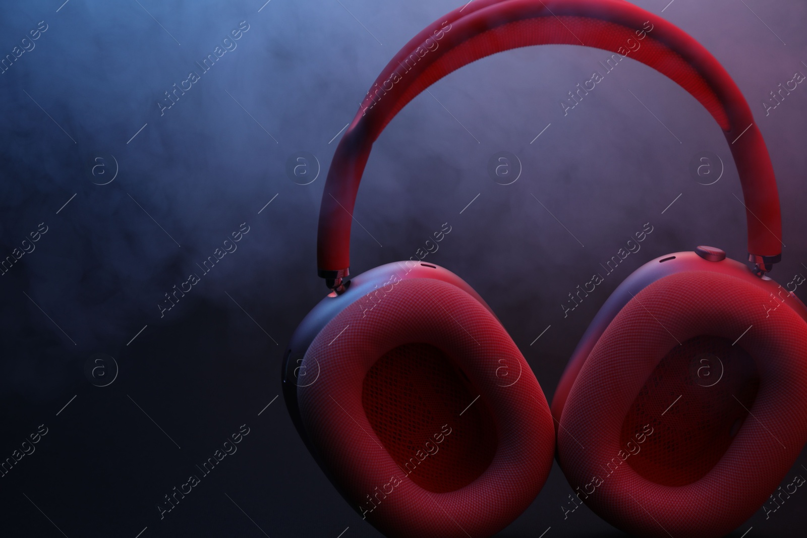 Pair of wireless headphones on dark background with color lights and smoke, closeup Photo of Pair of wireless headphones on dark background with color lights and smoke, closeup