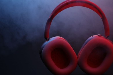 Photo of Pair of wireless headphones on dark background with color lights and smoke, closeup