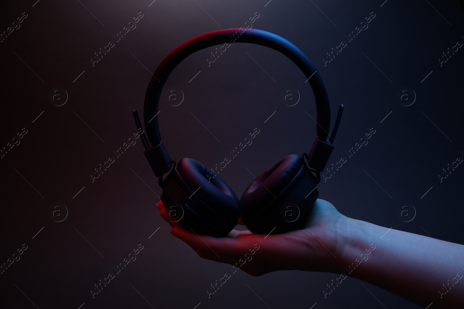 Woman holding wireless headphones on dark background, closeup Photo of Woman holding wireless headphones on dark background, closeup
