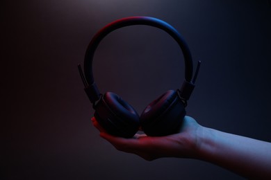Photo of Woman holding wireless headphones on dark background, closeup