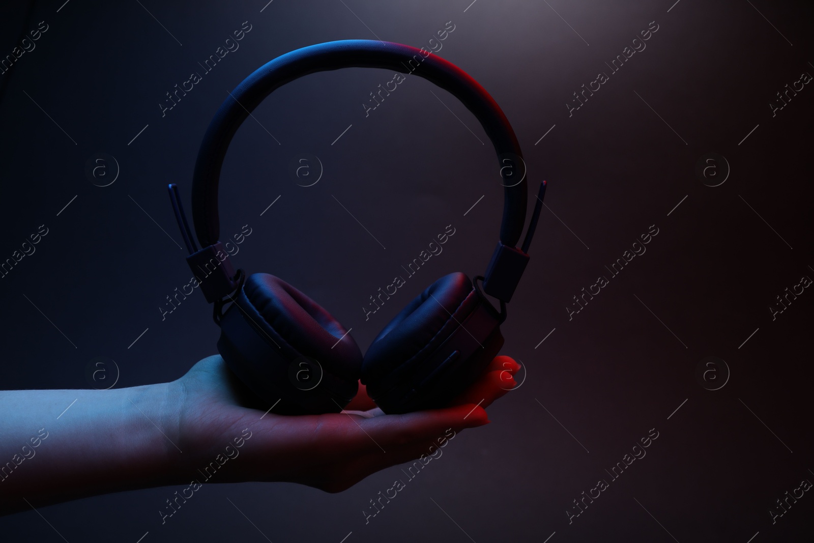 Woman holding wireless headphones on dark background, closeup Photo of Woman holding wireless headphones on dark background, closeup