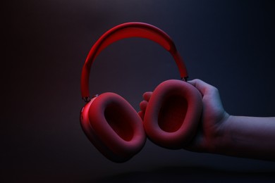Photo of Woman holding wireless headphones on dark background, closeup