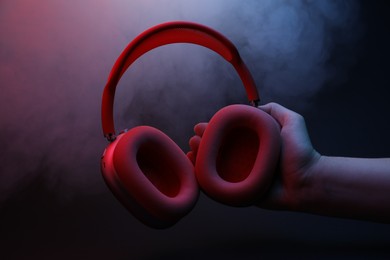 Photo of Woman holding wireless headphones on dark background with color lights and smoke, closeup